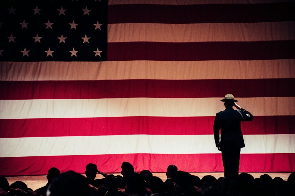 A solemn moment as a soldier salutes the American flag during a ceremony inside an auditorium.