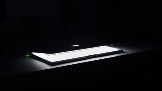 A dramatic, low-light image of a slightly open laptop with glowing keys on a dark desk.