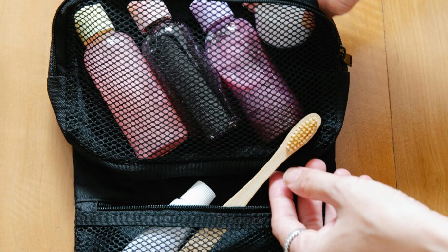 Open toiletry bag with bottles and a bamboo toothbrush on wooden surface.